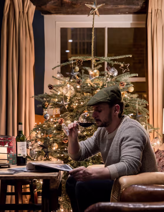 man drinking a glass of wine and reading a menu at a table beside a Christmas tree