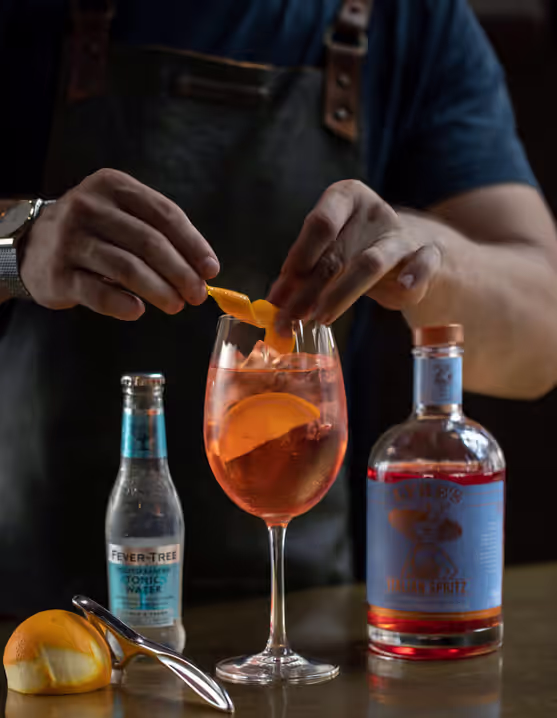 person adding orange peel twist into a glass of Amalfi Spritz