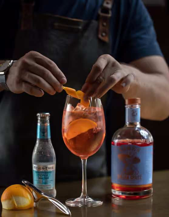 person adding orange peel twist into a glass of Amalfi Spritz