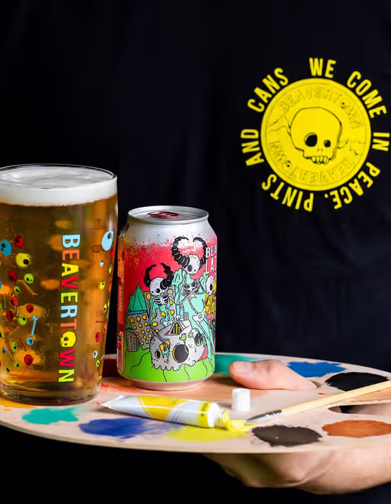 person holding a glass and can of Beavertown Lazer Crush AF IPA on a painting palette