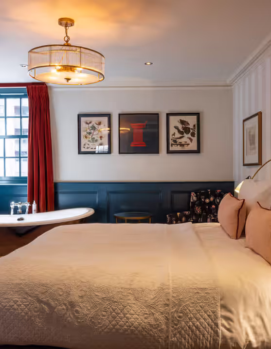 hotel room with freestanding bathtub, red curtains, and patterned armchair
