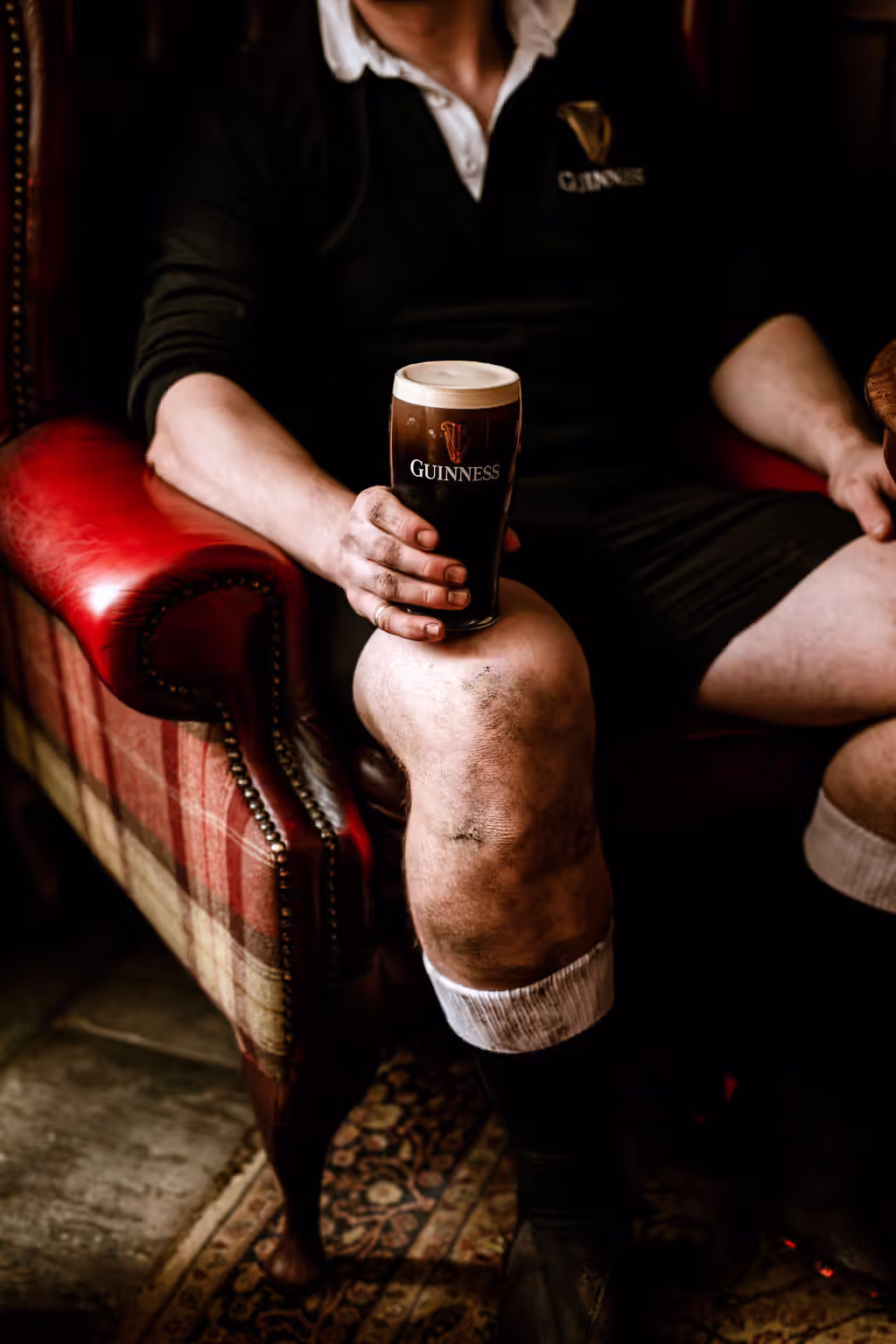 rugby player sitting in a red chair and holding a pint of Guinness on his knee