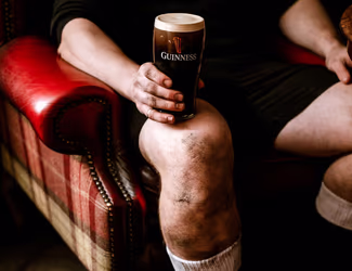 rugby player sitting in a red chair and holding a pint of Guinness on his knee