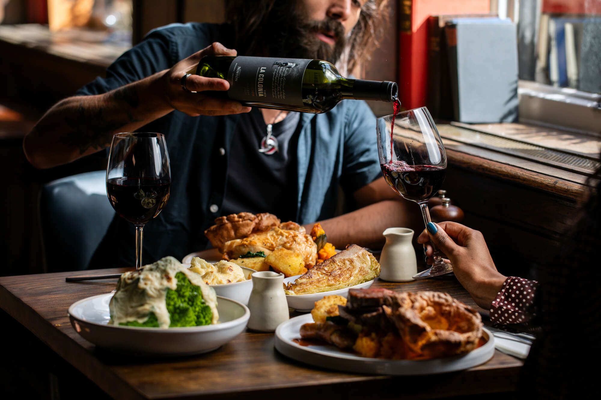 A man pouring a glass of red wine with a traditional British Sunday roast