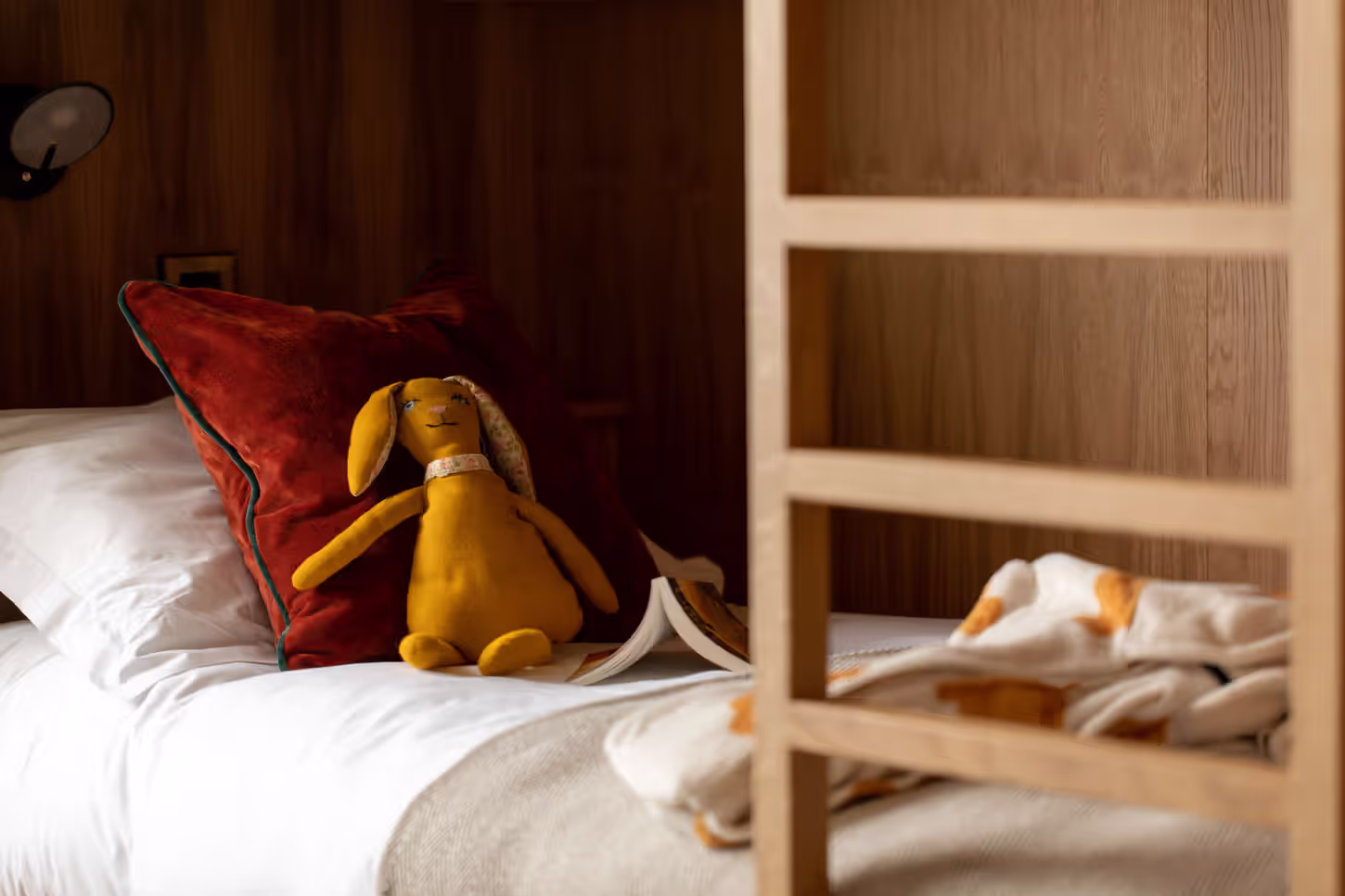 yellow stuffed bunny on a bunk bed with a book and a blanket