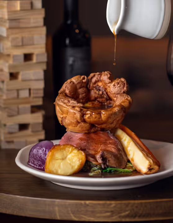 Sunday roast with Yorkshire pudding, gravy, and vegetables on a plate with a glass of red wine