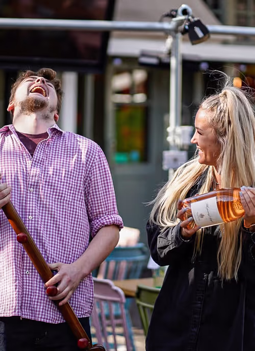 man holding an oar standing beside a woman holding a bottle of rosé