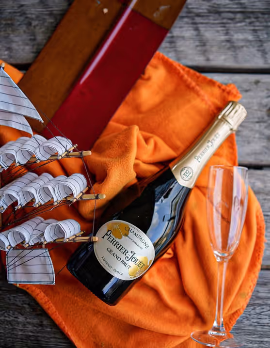Perrier Jouët champagne, glass, toy sailboat on an orange blanket