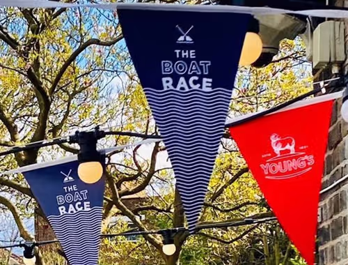 flags next to brick wall that say "The Boat Race" and "Young's"