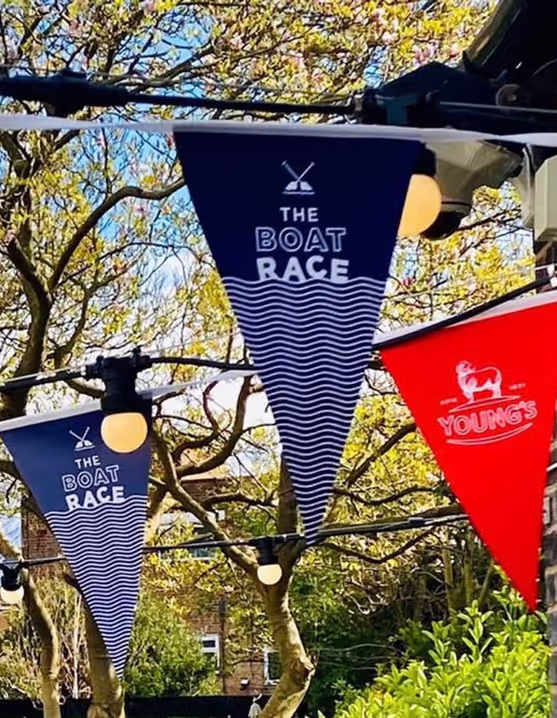 flags next to brick wall that say "The Boat Race" and "Young's"