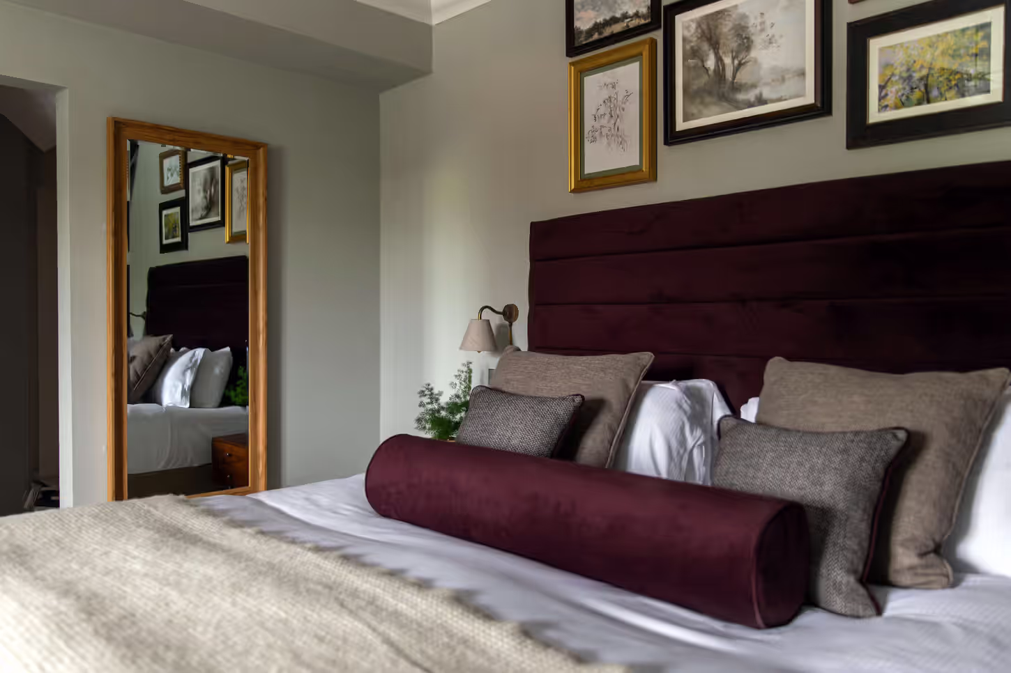 hotel bedroom with burgundy accents and pillows and framed paintings