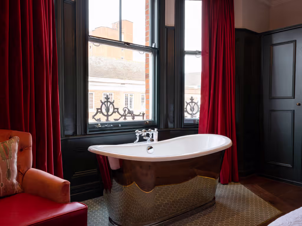 freestanding tub in front of a window with red curtains and a red armchair