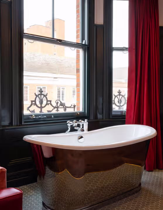 freestanding tub in front of a window with red curtains and a red armchair