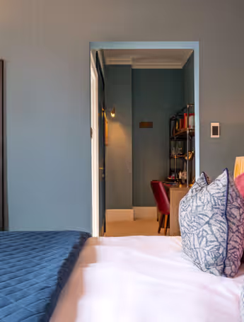 hotel room with a comfortable bed, patterned wallpaper, colourful pillows, and a desk area