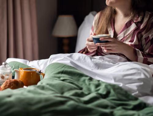 person lying in bed with a cup of tea