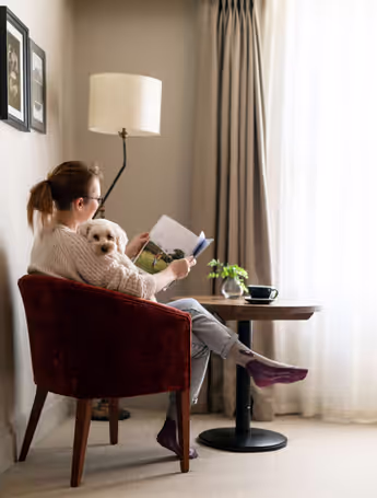 woman reading a magazine in a chair with a white dog on her lap