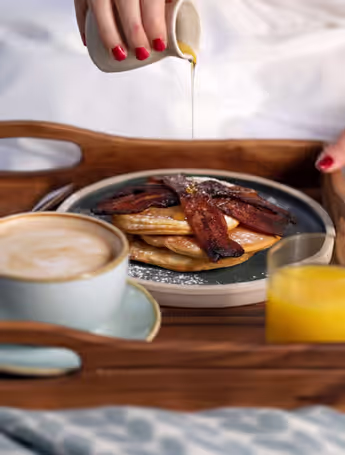 breakfast in bed on a tray with pancakes, bacon, coffee, and orange juice