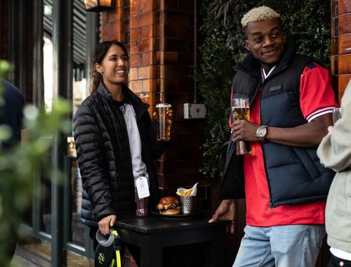 friends standing around a table with a tray of food while drinking Young's pints