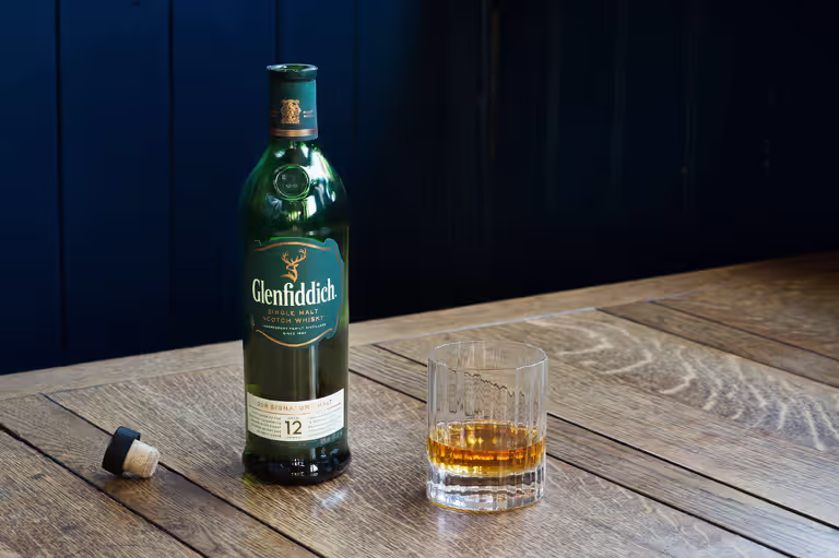 glass next to an open bottle of Glenfiddich single malt scotch whiskey