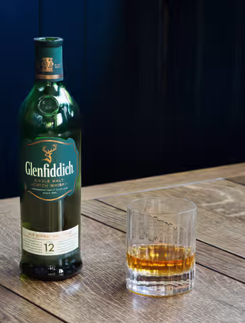 glass next to an open bottle of Glenfiddich single malt scotch whiskey
