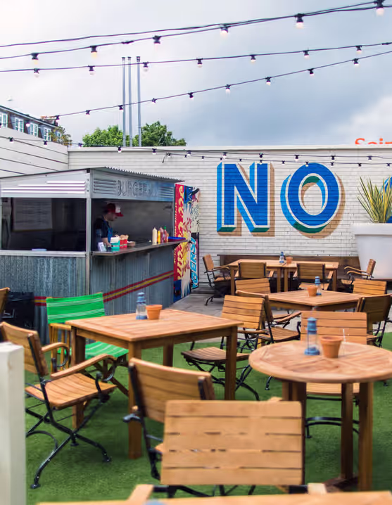 outdoor pub dining area with string lights, tables, chairs, and a burger shack