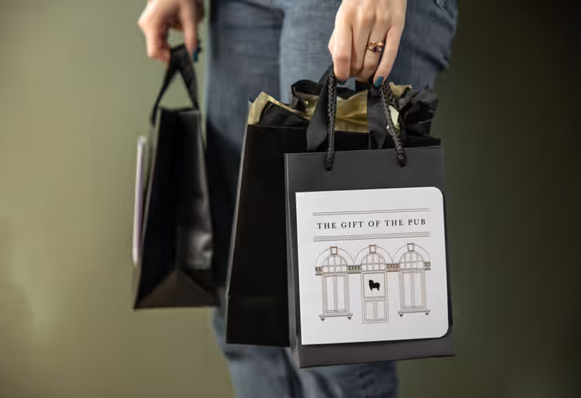 person holding two black bags that say the gift of the pub