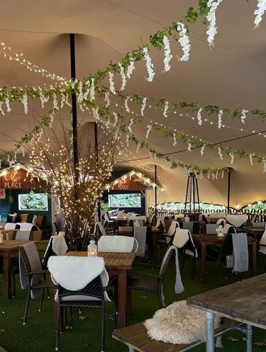 party tent with tables, chairs, lights, and floral garlands
