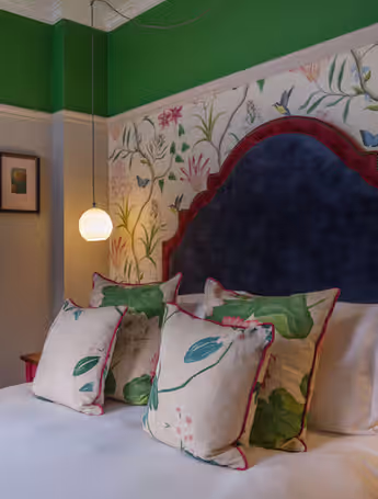 bed with colorful pillows and floral wallpaper in a cozy room