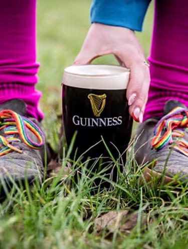 person holding a pint of Guinness in between their feet on the grass